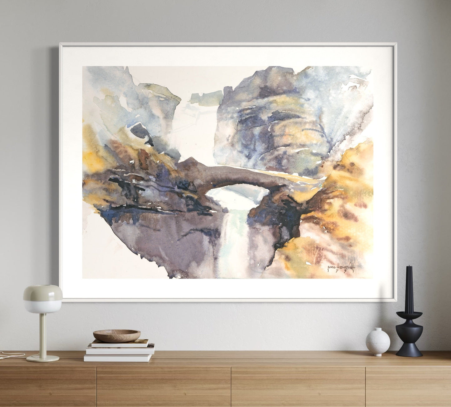 A framed watercolor painting depicting a abstract landscape in shades of gray, beige, and blue, hanging on a wall above a wooden console table.