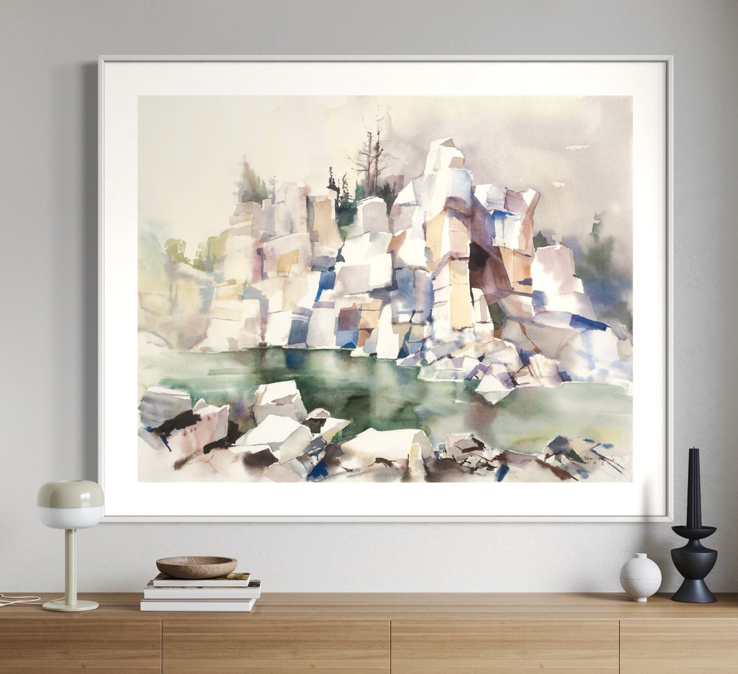 A framed watercolor painting titled 'Etrinkender Quarry' displayed on a wooden console table against a white wall, depicting abstracted rock formations in blue, beige, and green hues.