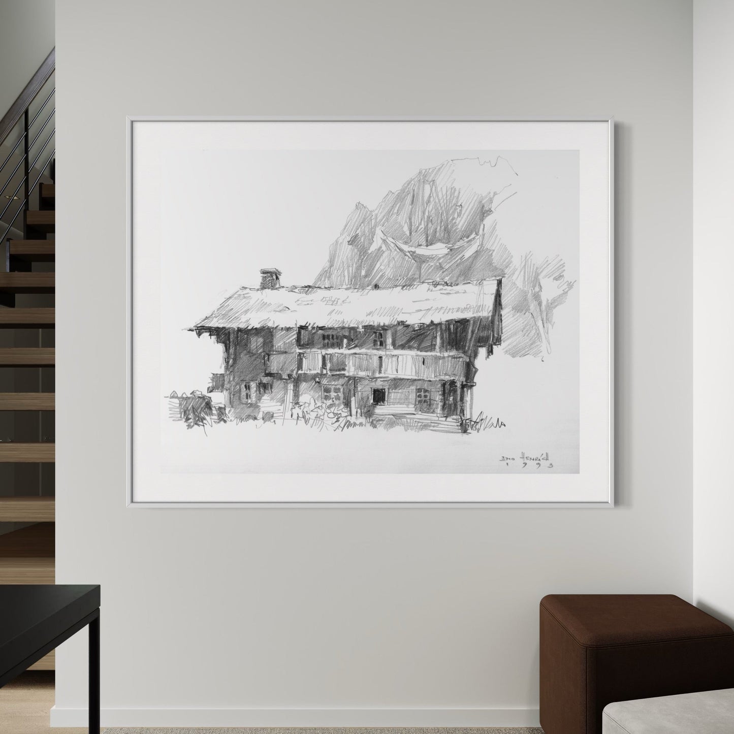 A framed black and white drawing of a mountainous landscape with a structure, displayed on a wall in a room with modern decor.