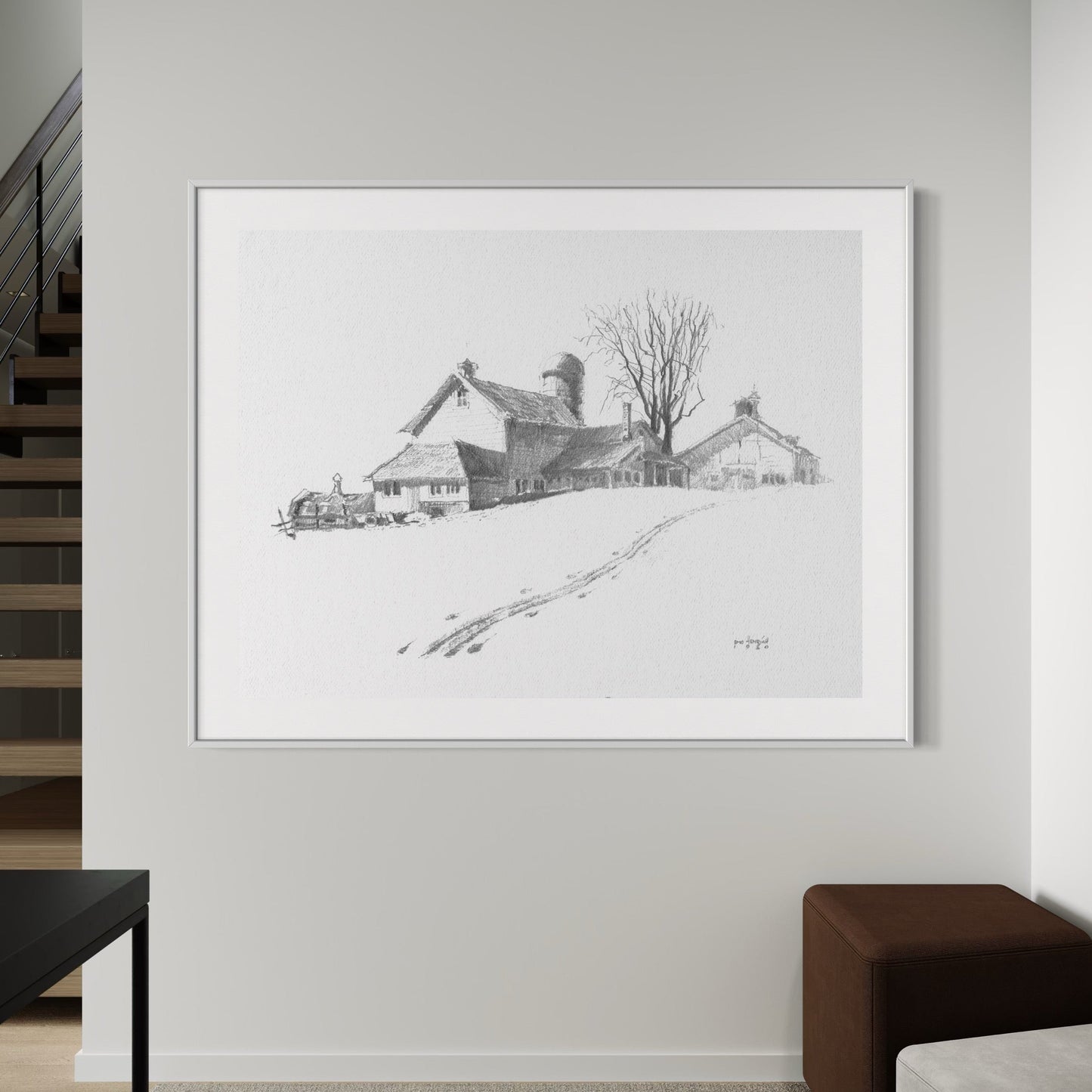 A framed and matted print of a graphite drawing depicting a barn, displayed on a wall in a home setting.