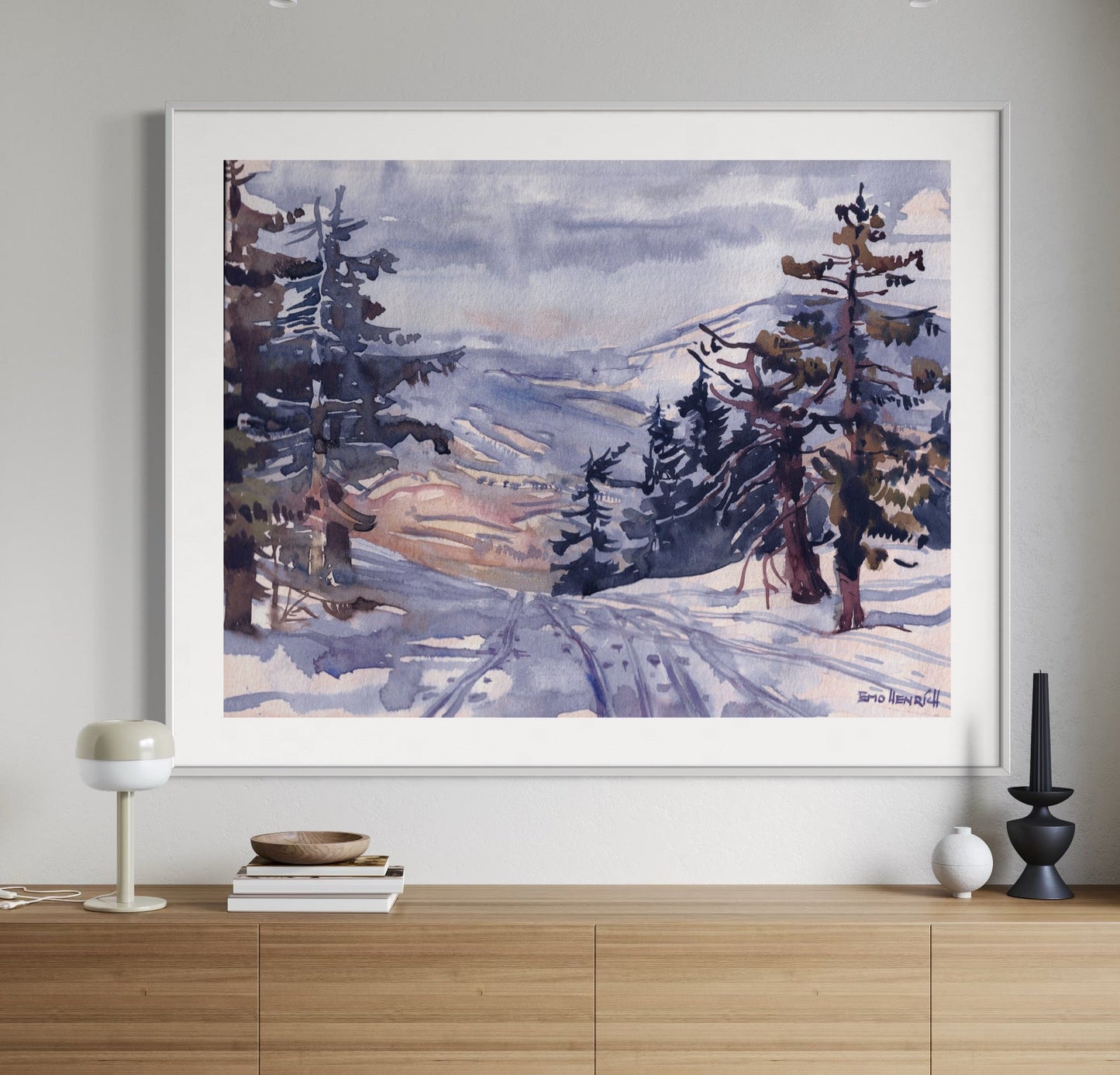A framed watercolor painting depicting a winter landscape with trees and a path covered in snow, displayed on a wooden console table.