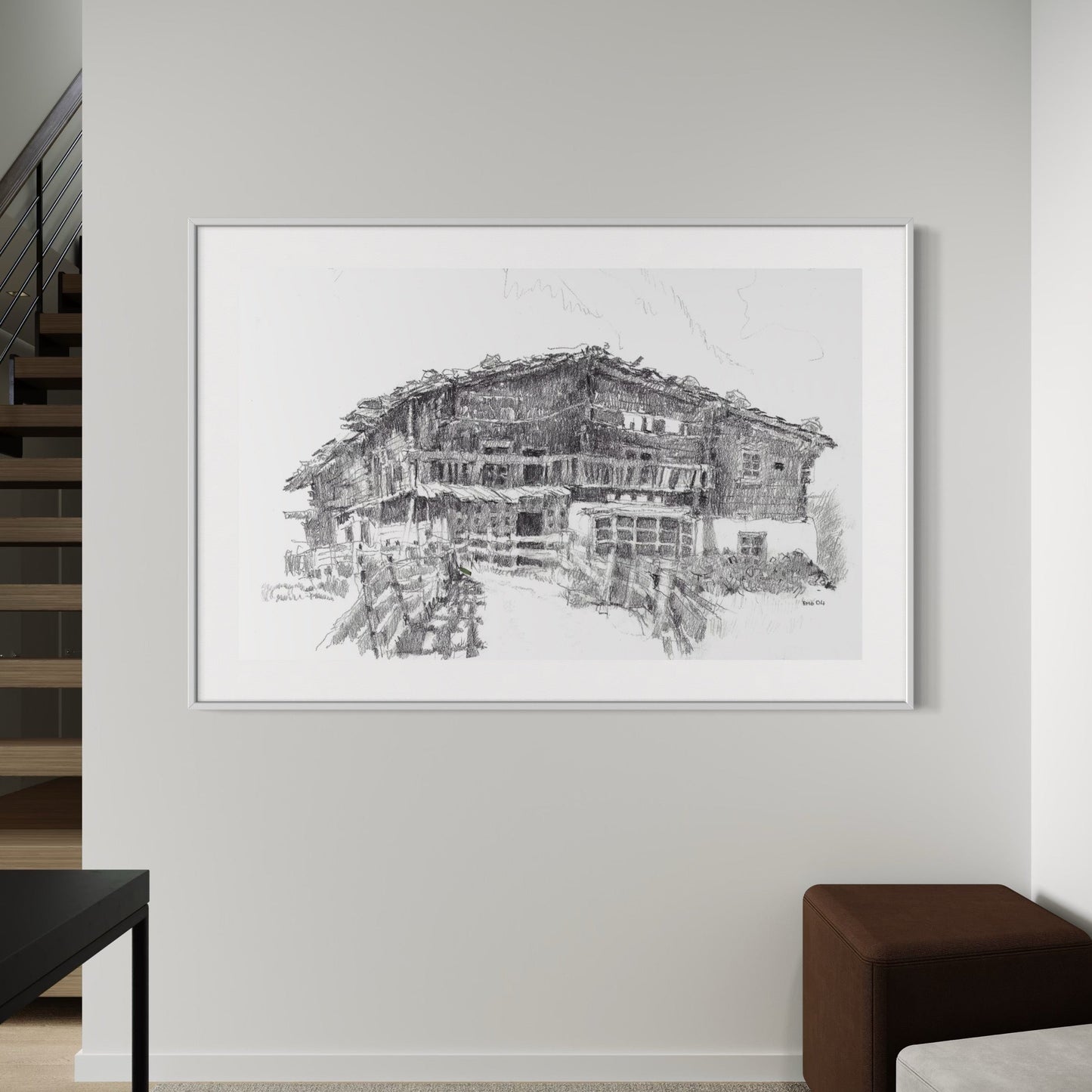 A graphite drawing of a farmhouses, titled 'Bauernhof Toni', displayed on a wall in a home setting, with a white frame.