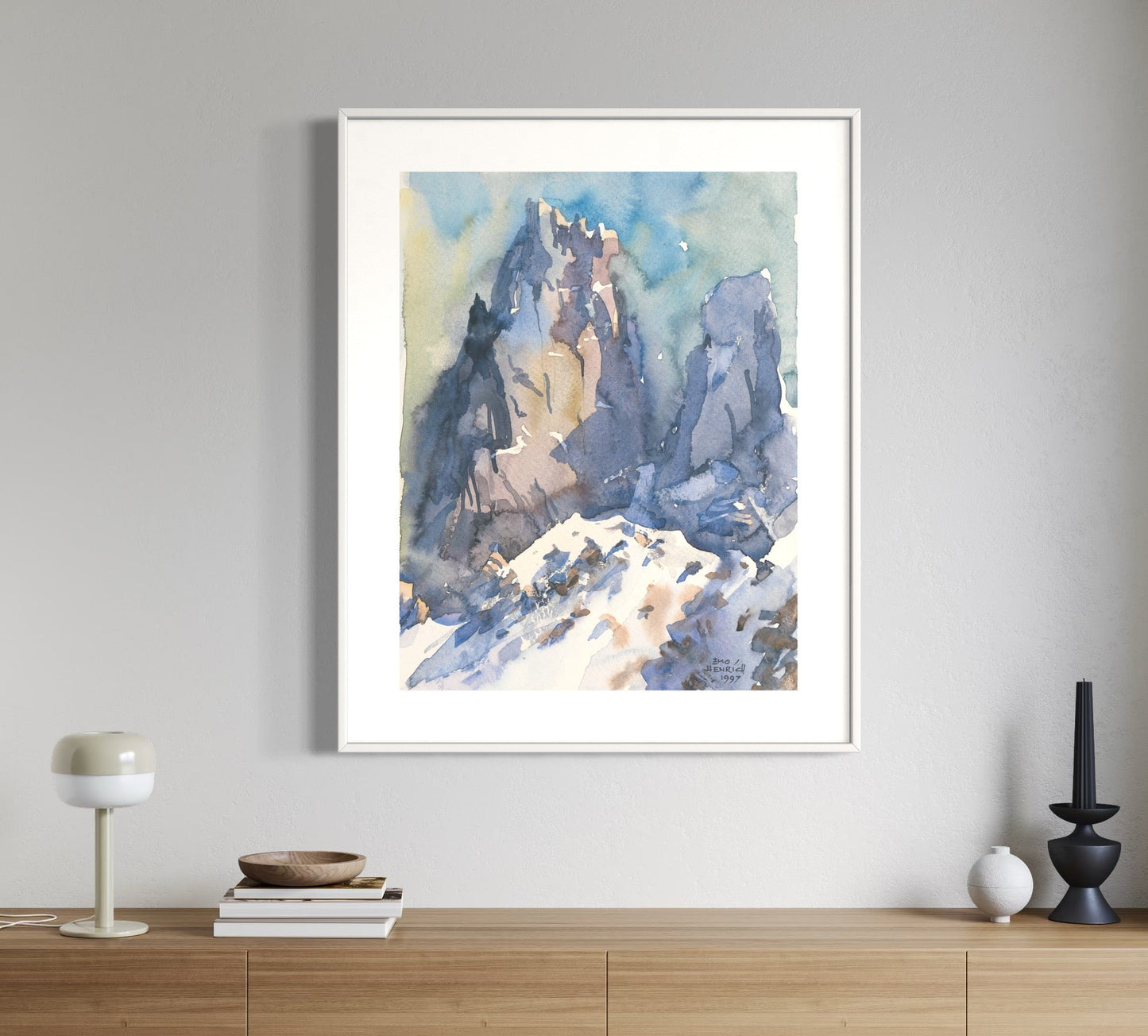 A framed watercolor painting of a mountainous landscape displayed on a wall.