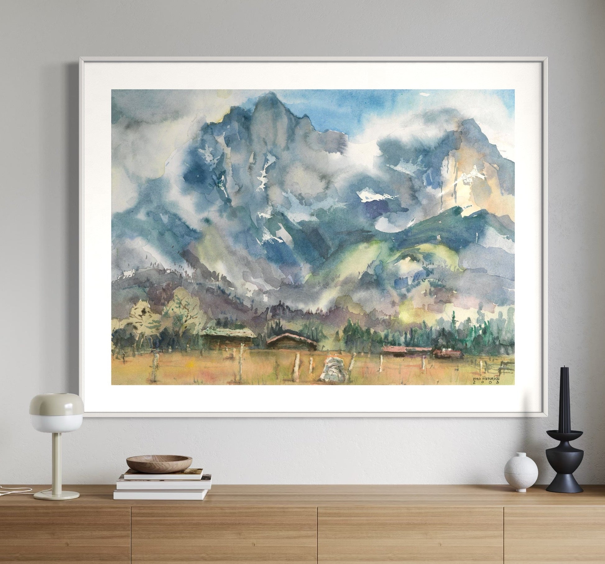 Framed artwork depicting a mountainous landscape with a watercolor technique, displayed on a wall.