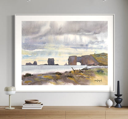 A framed watercolor painting of a cliffside scene, with a large door in the foreground, hanging on a white wall above a side table and chairs.