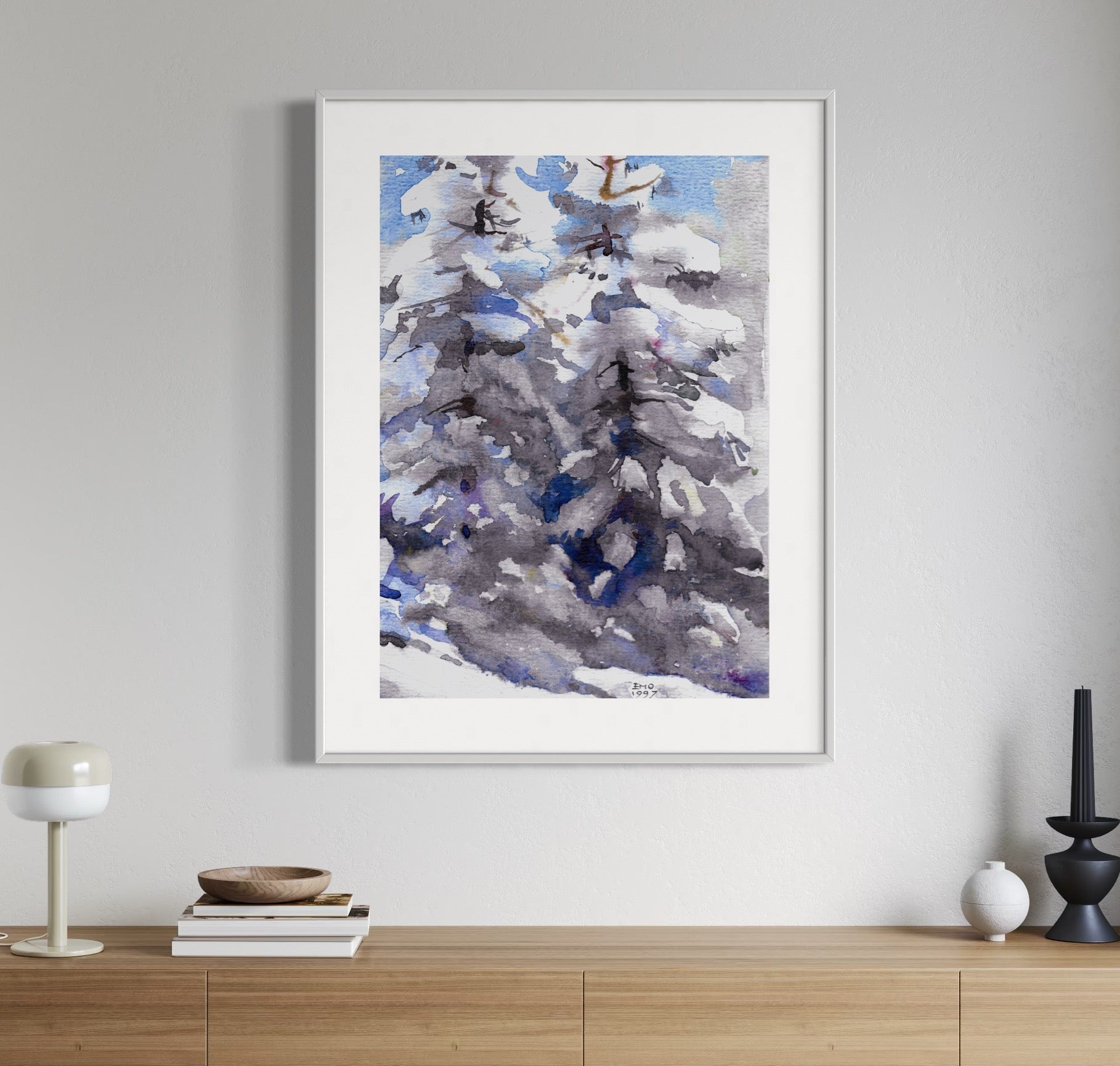 Framed watercolor painting of two trees covered in snow, displayed on a wooden console table against a white wall.