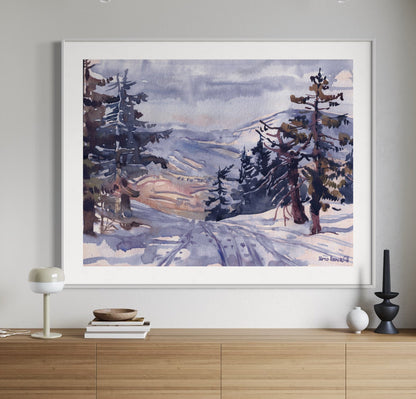 A framed watercolor painting depicting a winter landscape with trees and a path covered in snow, displayed on a wooden console table.